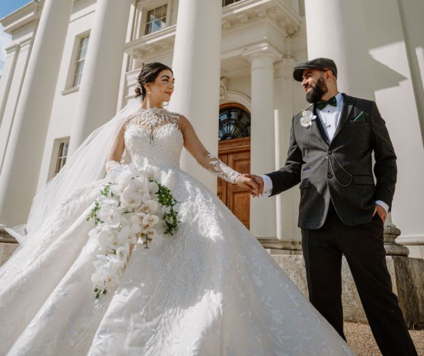 A couple holding hands in front of Hylands House. 