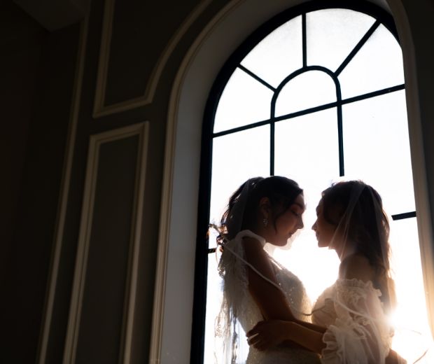 Two women wearing wedding dresses and embracing. 