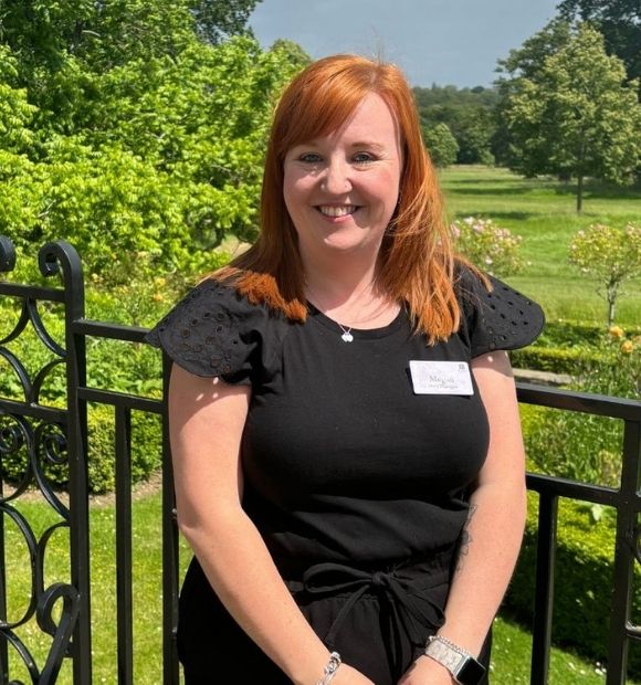 Megan, a woman with shoulder-length ginger hair, smiling while standing on the East Terrace. 