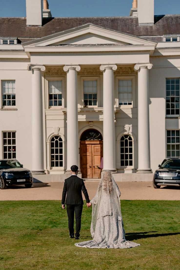 A couple holding hands outside Hylands House with their backs to the camera. 