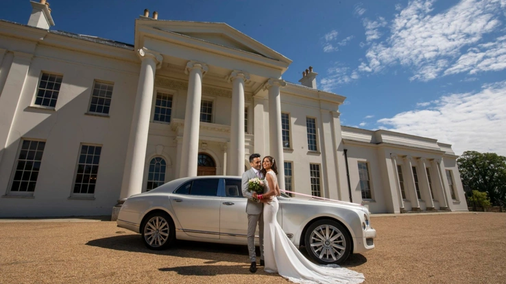 A couple standing in front of a luxury car outside of Hylands House. 