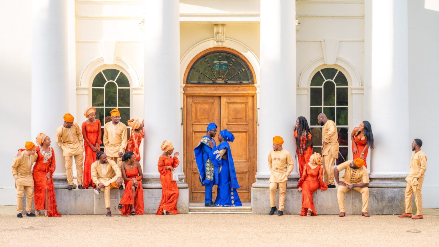 A couple embracing at the door of Hylands House while their wedding party look on. 