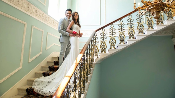 A bride and groom embracing on the Grand Staircase of Hylands House. 