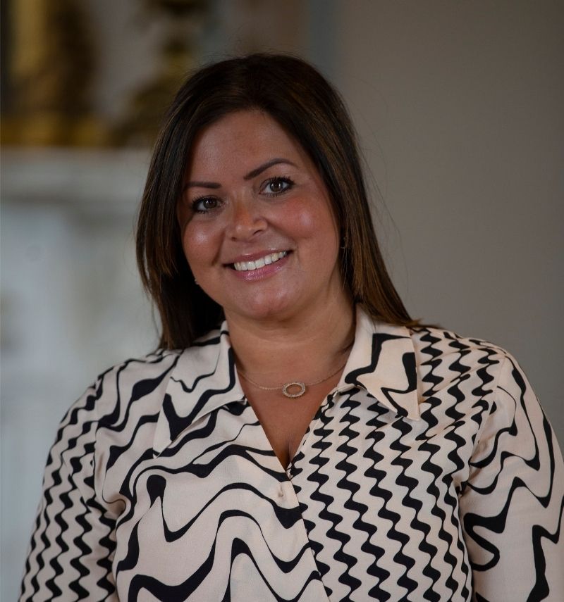 A woman with shoulder-length dark hair and a black and cream dress smiling at the camera. 