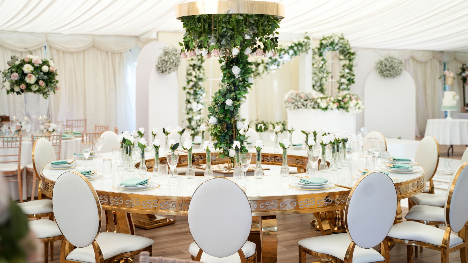 The Grand Pavilion decorated with gold circular tables and white and green florals. 
