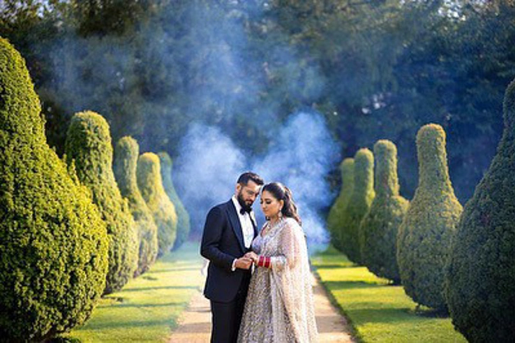 A couple holding hands while standing amongst the skittle hedges in the Pleasure Gardens. 