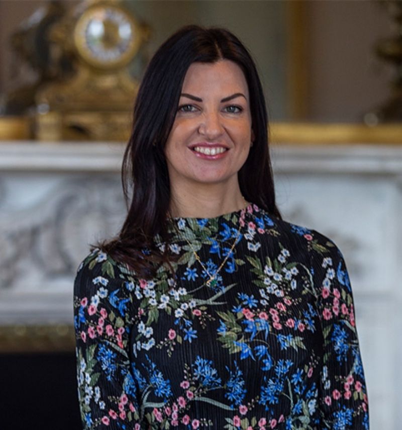 A woman with long dark hair and a floral dress smiling at the camera. 