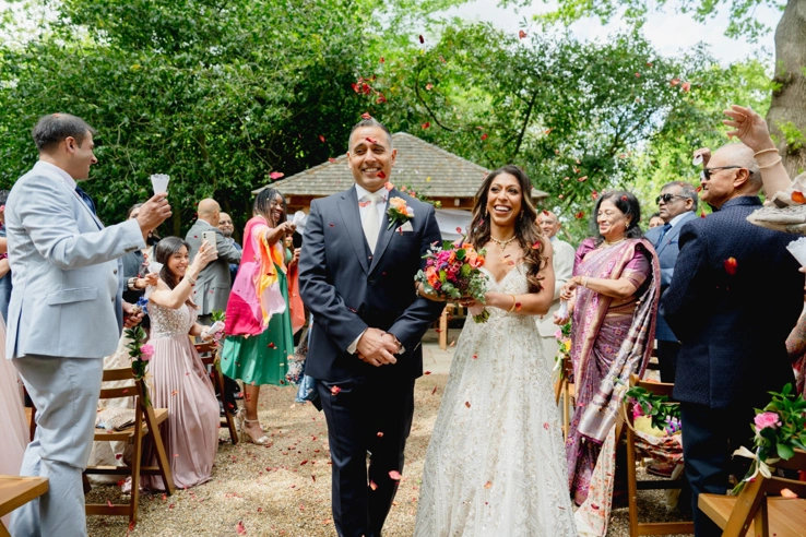 A couple walking up the aisle of the Outdoor Ceremony Garden while their guests toss confetti. 