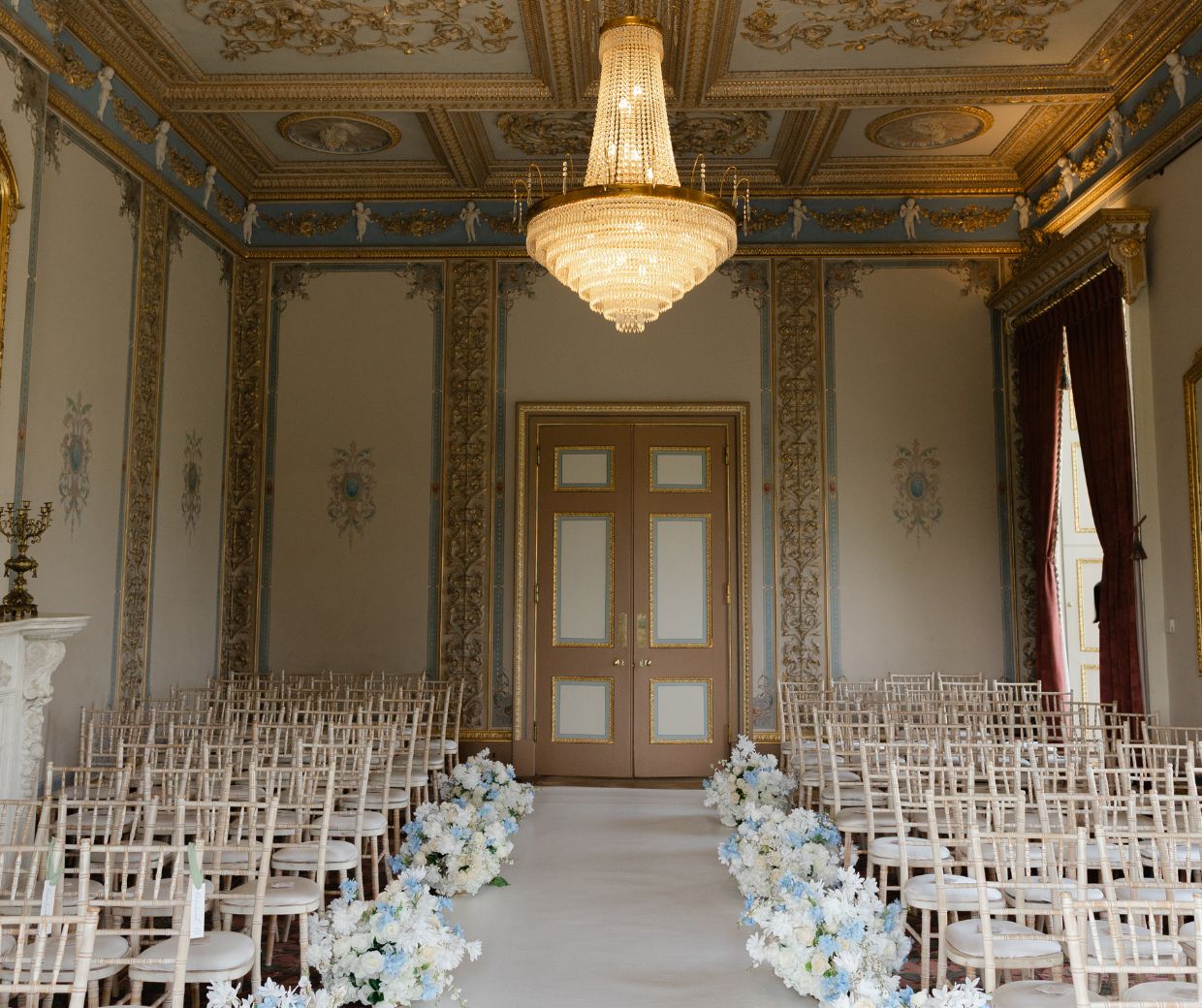 The Drawing Room of Hylands House set up for a wedding with a white runner laid down the aisle and pink and white flowers. 